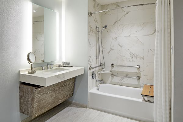 A modern bathroom features a well-lit mirror, a countertop with a small sink, and a bathtub with a shower and marble-style tiles.