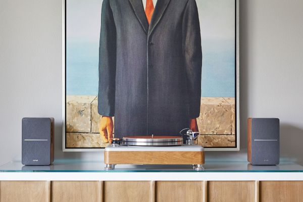 A framed painting of a man with an apple covering his face sits on a cabinet with speakers on either side.