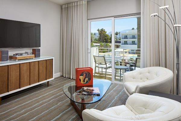 A modern living room with a TV, record player, chairs, coffee table, and balcony view through sliding doors.