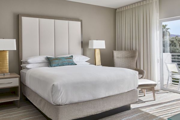 The image shows a modern bedroom with a large bed, two lamps, a chair, and a window with curtains and a view outside.