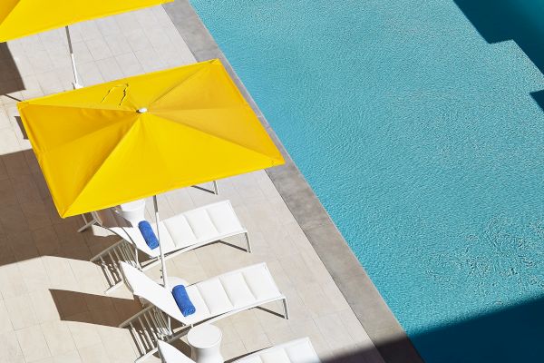 Poolside scene with yellow umbrellas and white lounge chairs near a clear blue pool, creating a sunny and inviting atmosphere.