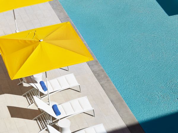 Poolside scene with yellow umbrellas and white lounge chairs near a clear blue pool, creating a sunny and inviting atmosphere.