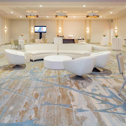 A modern, spacious meeting room with white sofas, round tables, chairs, and floral arrangements, set up for an event.