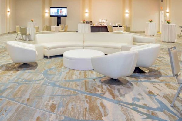 A modern event space with white couches arranged in a circle, patterned carpet, and tables in the background, including a screen.