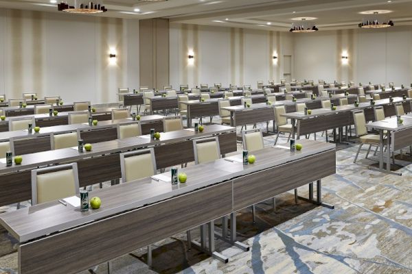 This image shows a conference room with rows of tables and chairs, set up for an event or meeting, with modern lighting fixtures.