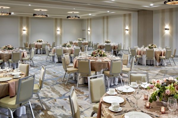 The image shows an elegantly decorated banquet hall set up with round tables, chairs, floral centerpieces, and tableware, ready for an event.