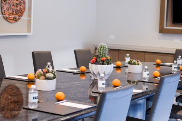 A conference room with a large table set with oranges, water bottles, cacti centerpieces, and chairs. Art decorates the white walls.