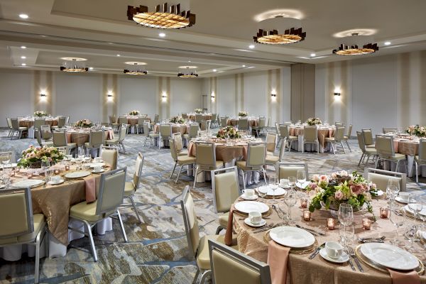 A banquet hall set up for an event, featuring round tables with floral centerpieces, table settings, and modern overhead lighting.