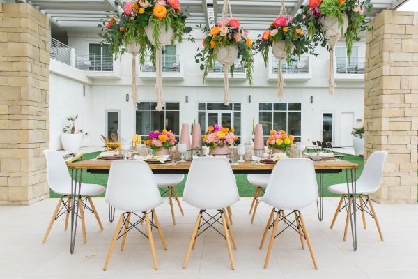 A beautifully set outdoor dining table with white chairs, floral arrangements, and hanging greenery, situated in a patio area.