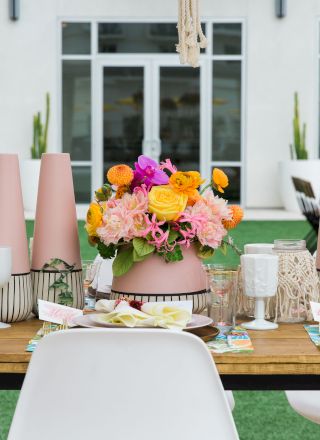 A beautifully set table with vibrant floral centerpieces and modern decor, outdoors in front of a building with large windows.