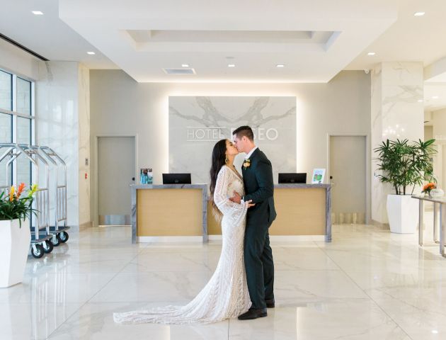 A couple is kissing in a hotel lobby, with elegant decor and plants around.