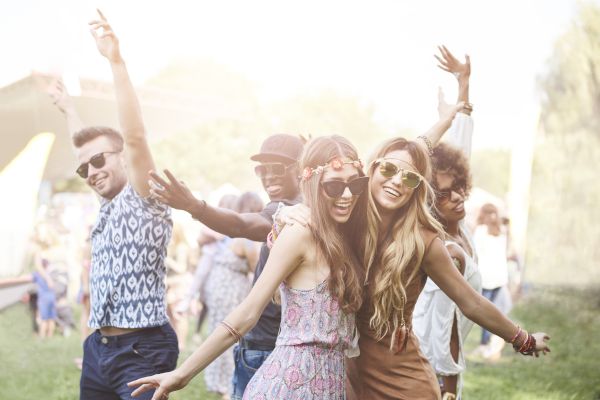 A group of people outdoors, smiling and posing playfully in casual summer attire, suggests they are enjoying a festive, sunny event.