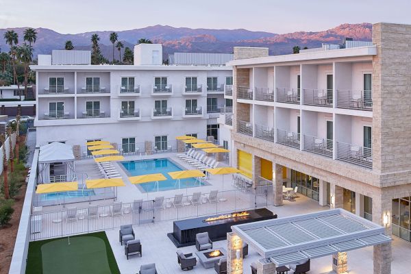 A modern hotel with a pool, yellow umbrellas, seating areas, and a small golf putting green, set against a mountainous backdrop.