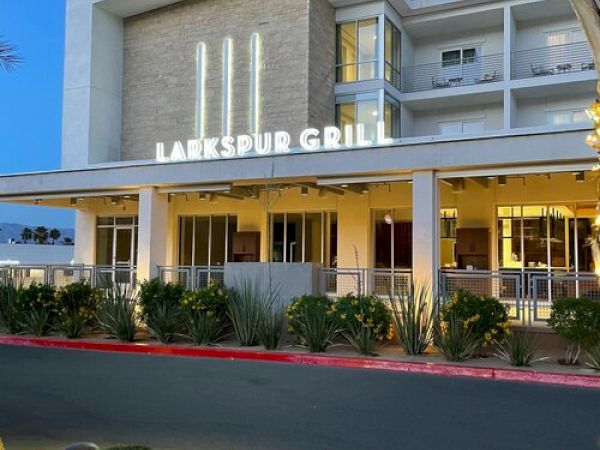 The image shows the exterior of Larkspur Grill, a modern building with illuminated signage and landscaping in front of it.