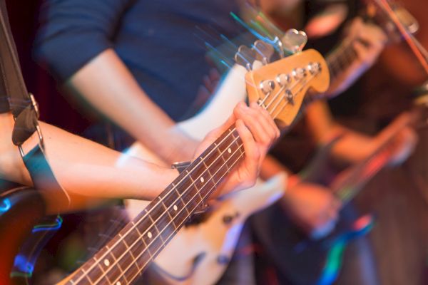 The image shows blurred motion of musicians playing electric guitars, capturing dynamic movement and energy during a live performance.