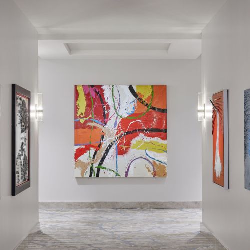 A hallway with several abstract paintings on the walls, featuring vibrant colors and dynamic patterns.