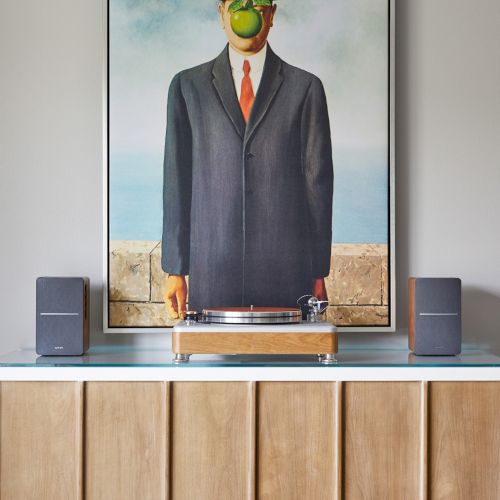 A painting of a man in a suit with an apple in front of his face above a turntable on a wooden cabinet with speakers.