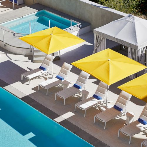 The image shows a poolside area with yellow umbrellas, lounge chairs, two cabanas, and a hot tub, creating a relaxing atmosphere.