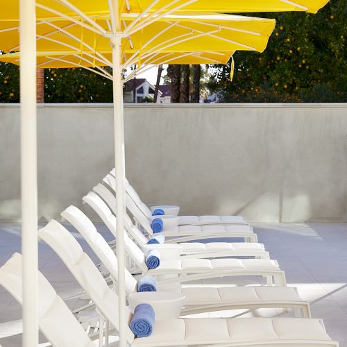 White lounge chairs with blue towels are lined up beneath large yellow umbrellas.