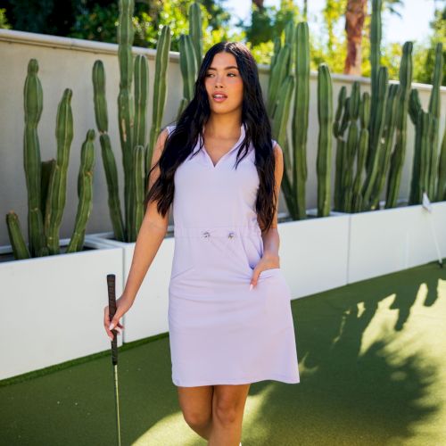 A woman in a sleeveless dress holds a golf club, standing on a golf course with cactus plants in the background.