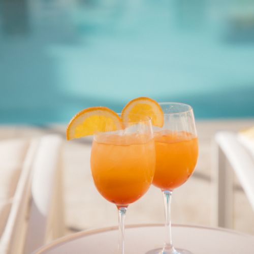 Two glasses of orange cocktails with orange slices on a small table by a pool.