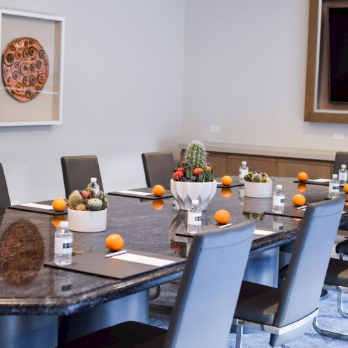 A conference room with a long table, chairs, bottles of water, oranges, notepads, and decorative plants on the table.